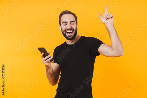 Image of attractive man in earpods listening to music with cellphone