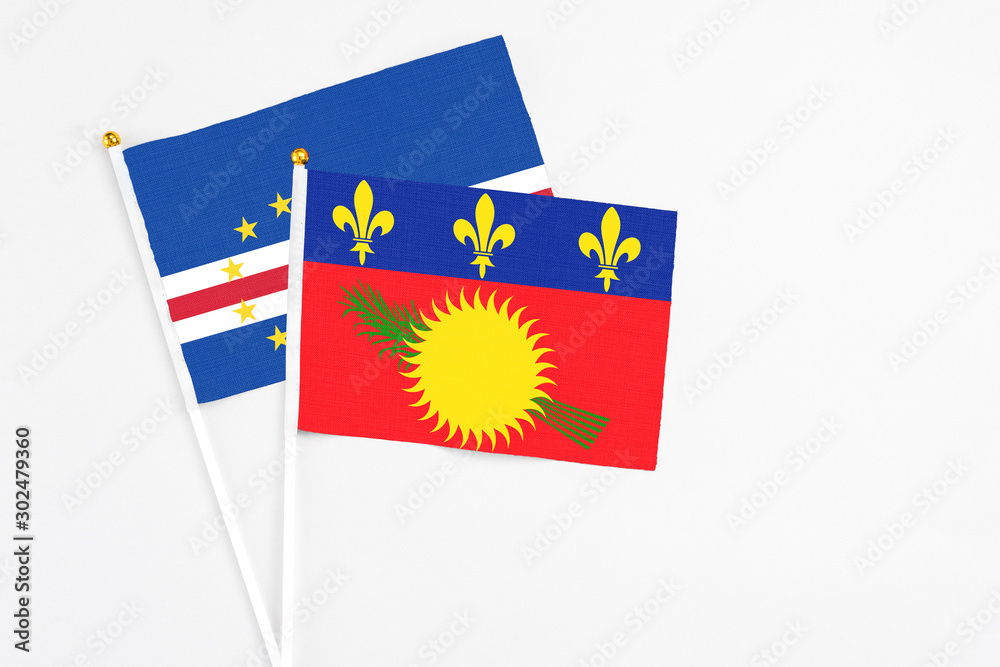 Naklejka premium Guadeloupe and Cape Verde stick flags on white background. High quality fabric, miniature national flag. Peaceful global concept.White floor for copy space.
