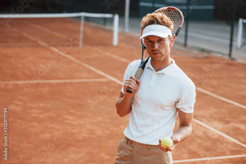 Holds ball in hand. Young tennis player in sportive clothes is on the court outdoors © standret