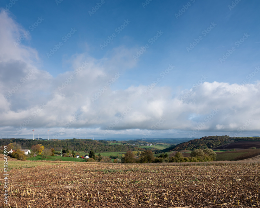 rural landscape with colorful forest in german eifel under cloudy sky in the fall