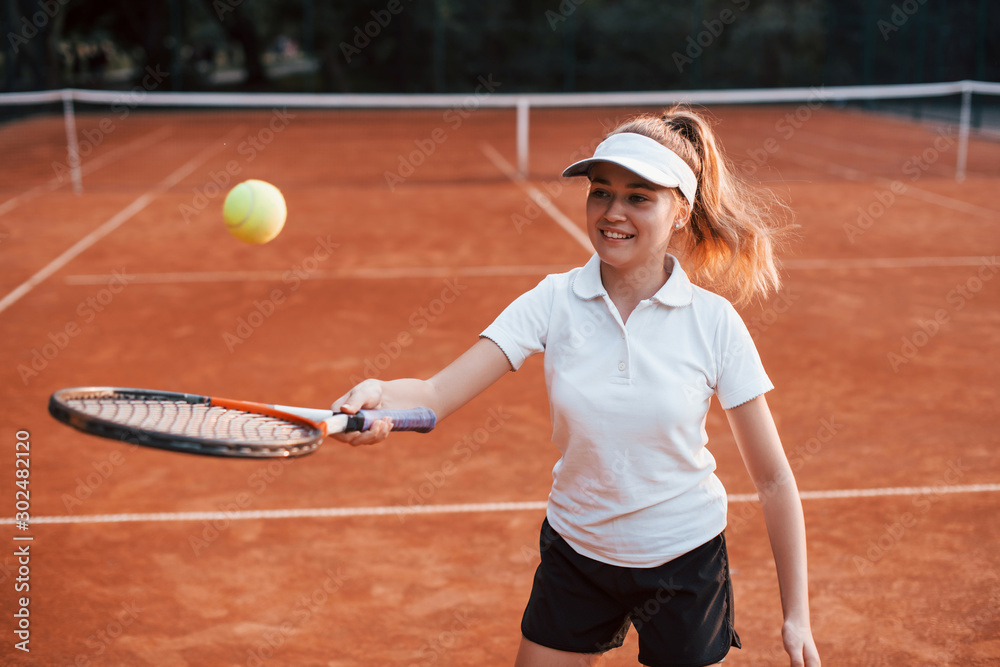 Young female tennis player in sportive clothes is on the court outdoors
