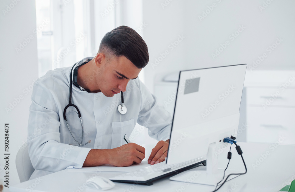 Working with documents. Young stylish male doctor with stethoscope is in clinic at daytime Working with documents. Young stylish male doctor with stethoscope is in clinic at daytime