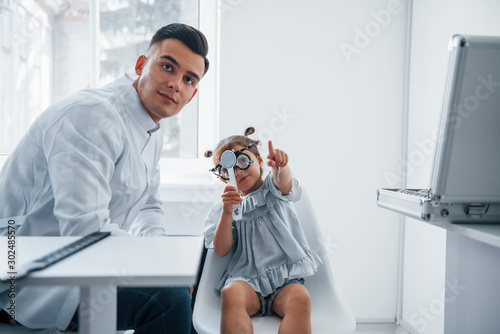 Testing vision. Young ophthalmologist is with little female visitor in the clinic photo