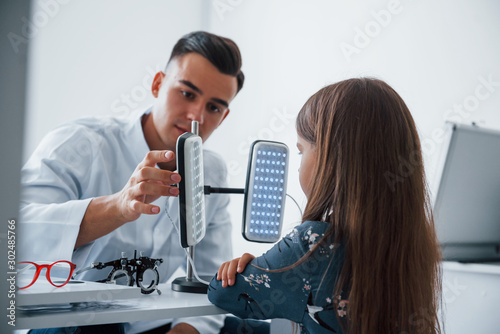 Two panels on the table. Young ophthalmologist is with little female visitor in the clinic photo