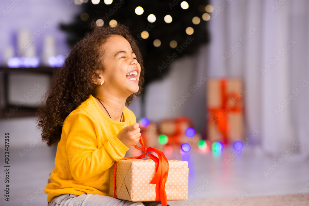 Excited african girl laughing with Christmas gift - obrazy, fototapety, plakaty 