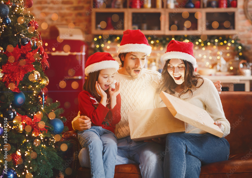 Emotional young family opening big box next to Christmas tree