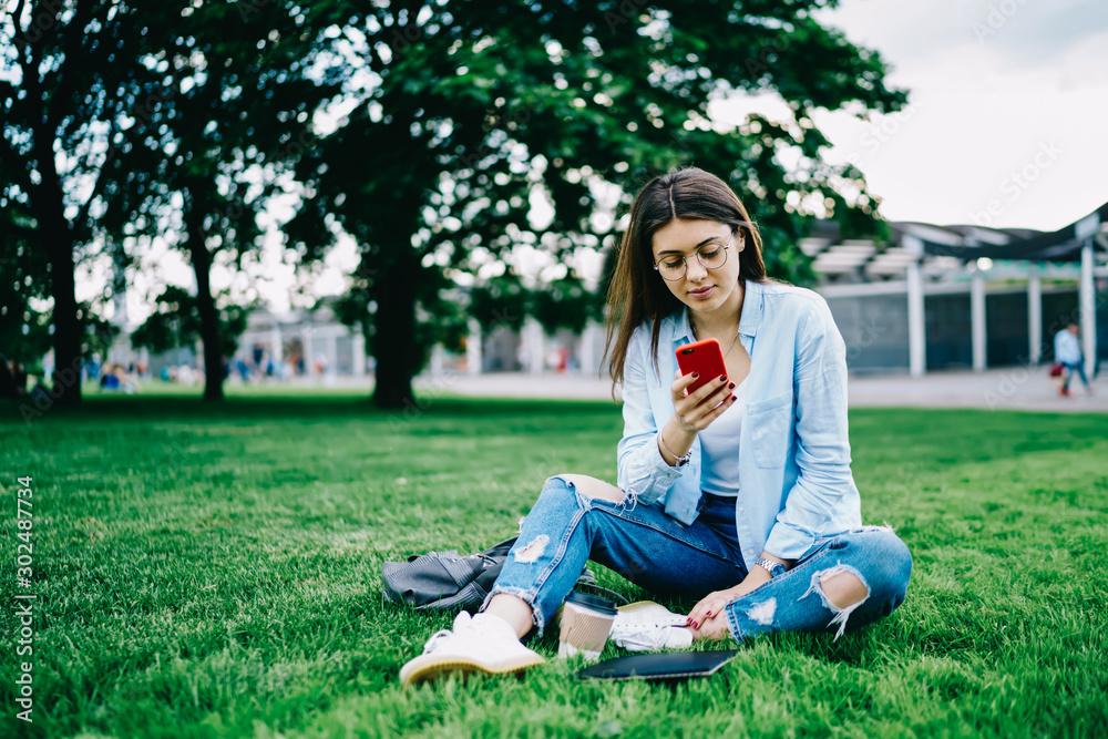 Teen hipster girl checking mail and publicating new post in networks via smartphone on free time in park, young woman recreating on green grass using mobile phone for chatting and reading news Teen hipster girl checking mail and publicating new post in networks via smartphone on free time in park, young woman recreating on green grass using mobile phone for chatting and reading news