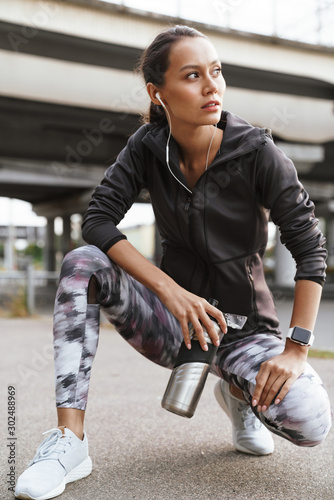 Image of young athletic woman drinking water while squatting