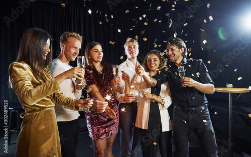 Group of cheerful friends celebrating new year indoors with drinks in hands