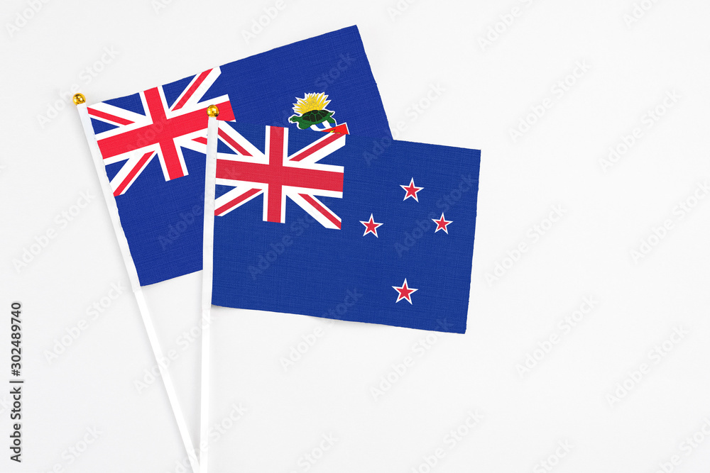 Fototapeta premium New Zealand and Cayman Islands stick flags on white background. High quality fabric, miniature national flag. Peaceful global concept.White floor for copy space.