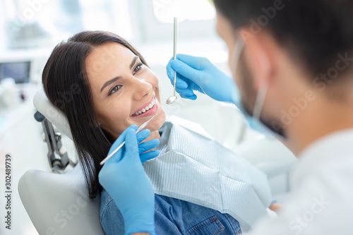 smiling happy client in dental chair with doctor looking her with instruments