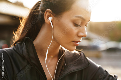 Image closeup of young focused woman using earphones while working out