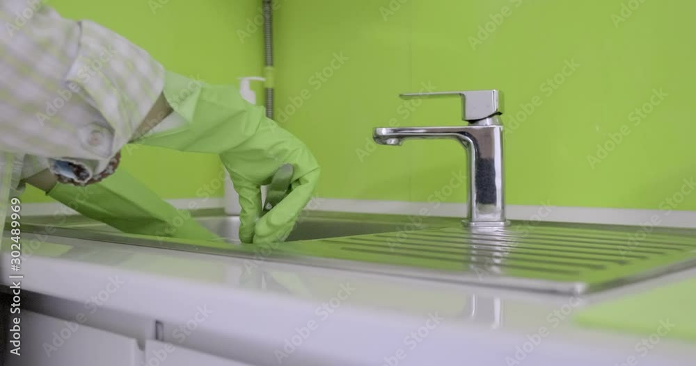 Mature woman in rubber gloves washing dishes in the kitchen with sponge