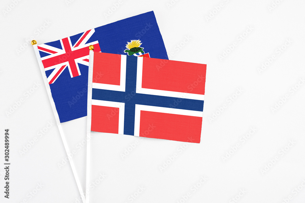 Fototapeta premium Norway and Cayman Islands stick flags on white background. High quality fabric, miniature national flag. Peaceful global concept.White floor for copy space.