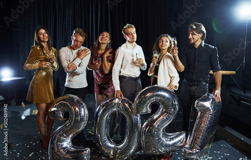 Cheerful group of people with drinks and balloons in hands celebrating new 2021 year
