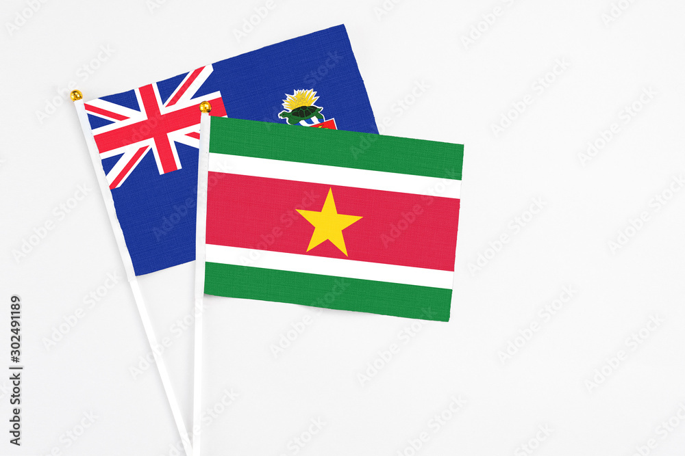 Naklejka premium Suriname and Cayman Islands stick flags on white background. High quality fabric, miniature national flag. Peaceful global concept.White floor for copy space.