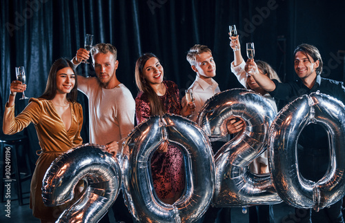 Cheerful group of people with drinks and balloons in hands celebrating new 2020 year