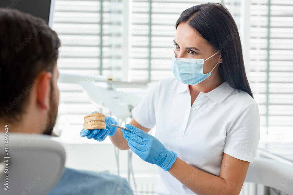 female doctor showing jaws model to male client sitting in dental chair female doctor showing jaws model to male client sitting in dental chair