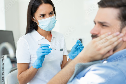 upset client touching face while having toothache near dentist in the hospital