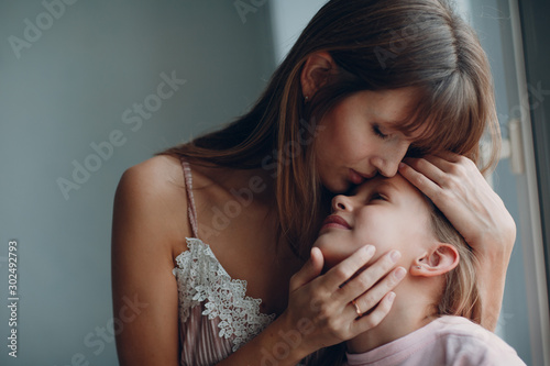 Mother hug with a little daughter at window. Family and mother's day concept.