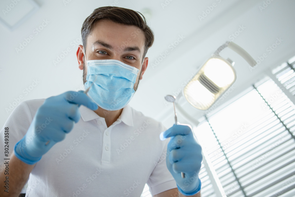 low angle view of male dentist checking patient teeth with mirror in modern clinic low angle view of male dentist checking patient teeth with mirror in modern clinic