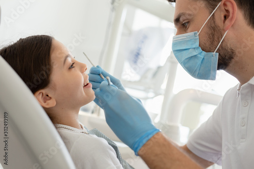 male doctor with instruments in the hands with girl sitting in the dental chair