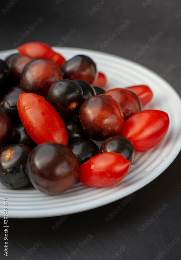 Red and black tomatoes on white plate. Black skinned tomatoes with crimson flesh Red and black tomatoes on white plate. Black skinned tomatoes with crimson flesh