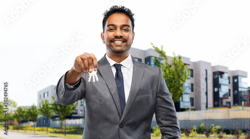 real estate business and people concept - indian man realtor with keys over living houses on city street background