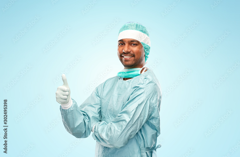 medicine, surgery and people concept - smiling indian male doctor or surgeon in protective wear showing thumbs up over blue background medicine, surgery and people concept - smiling indian male doctor or surgeon in protective wear showing thumbs up over blue background