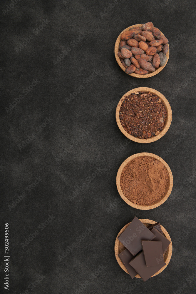 Fototapeta premium organic cacao beans, cocoa powder, ground and chocolate on a black background with copy space for text. Flat lay, top view. Ingredient. Vegan food. Background, pattern, card, menu. Vertical photo.