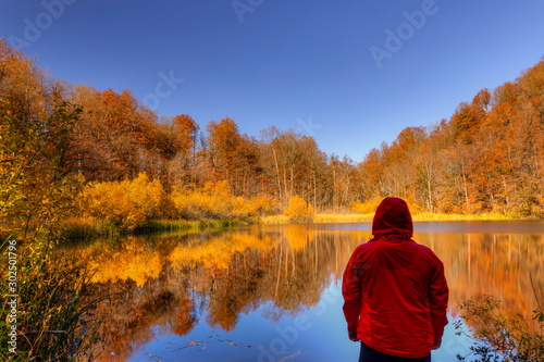 Hiker overlooking a small mountain lake while in the autumn forest photo