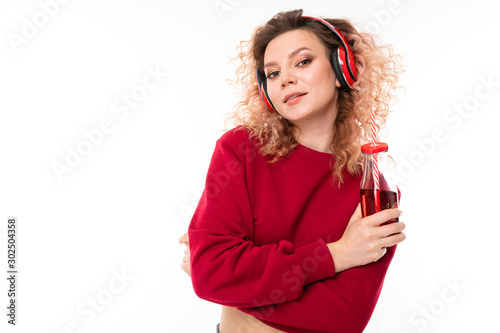 Caucasian girl with curly fair hair drinks juice and listen to music, portrait isolated on white background