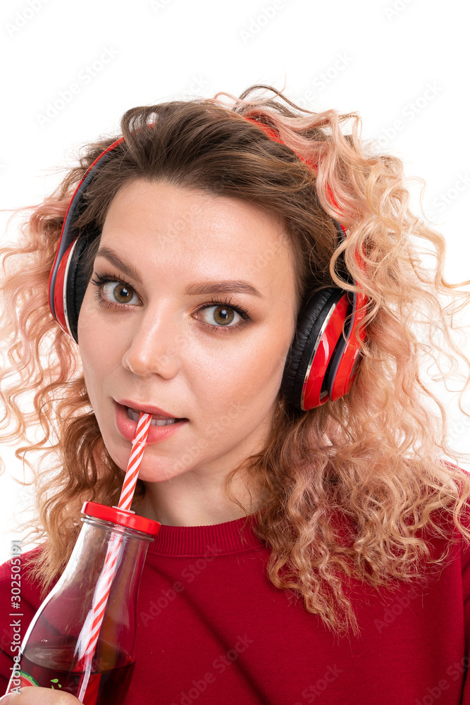 Caucasian girl with curly fair hair drinks juice and listen to music, portrait isolated on white background Caucasian girl with curly fair hair drinks juice and listen to music, portrait isolated on white background