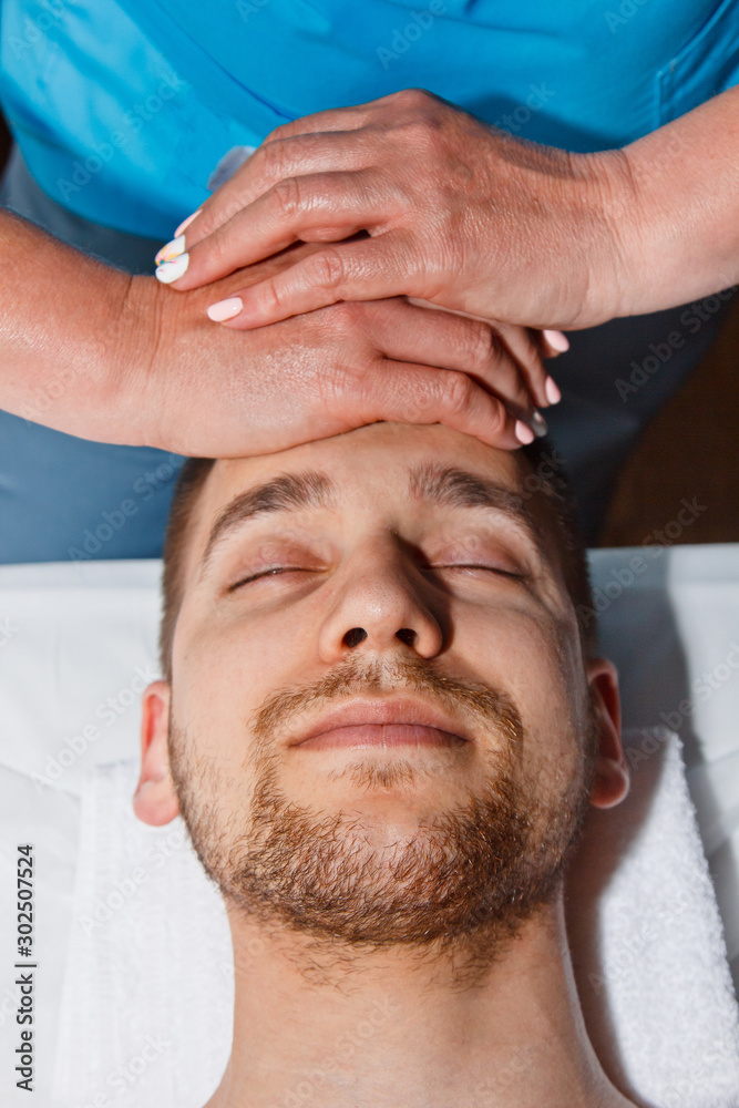Obraz premium Wellness concept. Professional masseur gives a man a Thai facial massage with special sticks in a spa center. Relaxation and recovery after work.
