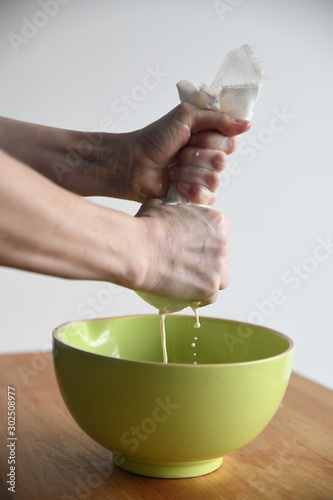 Hands wringing out a cheesecloth into a green bowl photo