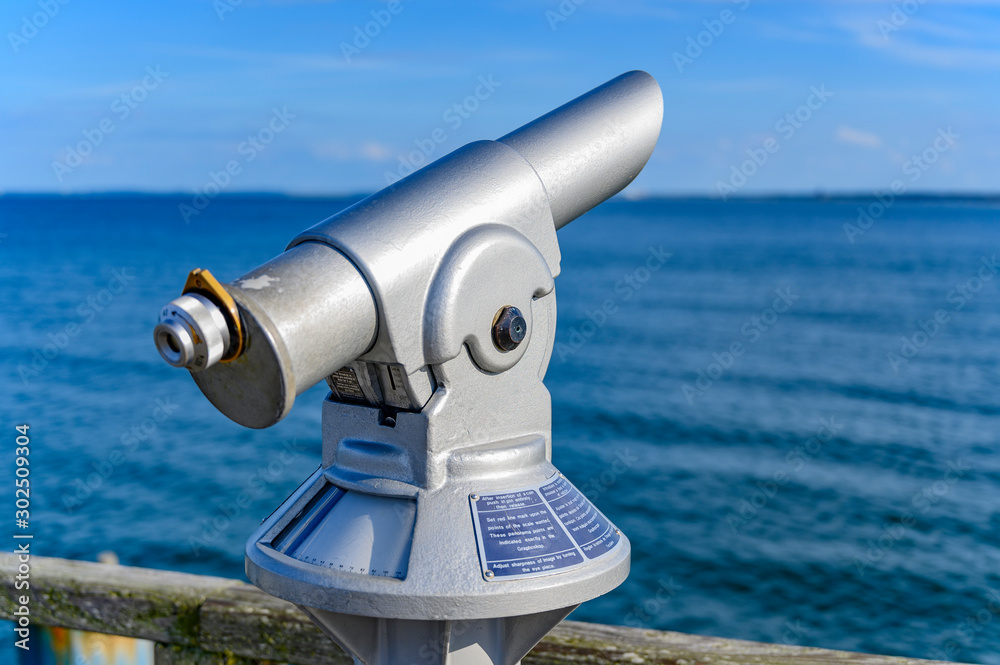 Telescope with coin slot on the pier in Bansin on the island of Usedom in Germany. Sea and sky are dark blue and radiate in the sunshine.