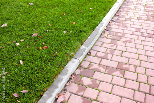 Styling paving slabs. Red paving slab next to a luxurious green lawn.