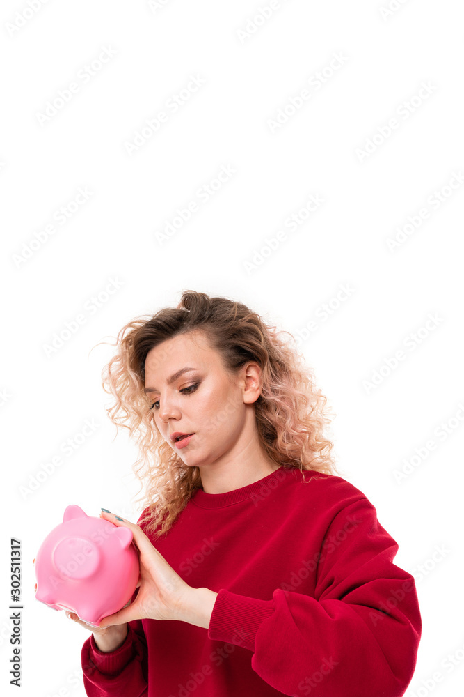 Caucasian girl with curly fair hair trying to get money from the pink pig moneybox, portrait isolated on white background Caucasian girl with curly fair hair trying to get money from the pink pig moneybox, portrait isolated on white background