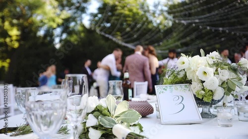 Fashionable wedding table decoration with white flower bouquets of roses and eustoma slow motion closeup, outdoor restaurant background