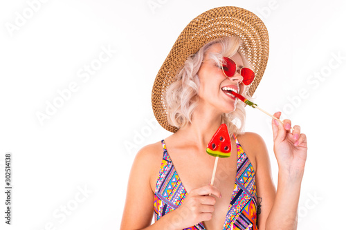 Happy blonde caucasian female stands in swimsuit with watermelon lolipops and smiles isolated on white background photo