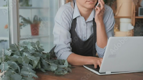 Female florist working on laptop and phone at flower shop