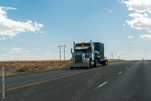 A truck crosses the desert lands of Utah under a blue and cloudy sky