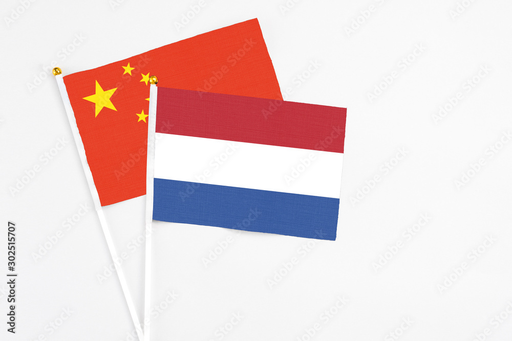 Netherlands and China stick flags on white background. High quality fabric, miniature national flag. Peaceful global concept.White floor for copy space. Netherlands and China stick flags on white background. High quality fabric, miniature national flag. Peaceful global concept.White floor for copy space.
