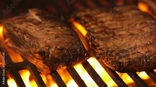 A few delicious pork or beef steaks are grilled over a live fire. Classic foods preparation. Pork steak on flaming grill barbecue. Gourmet cooking roasted meat. Cook in picnic. Organic food processing