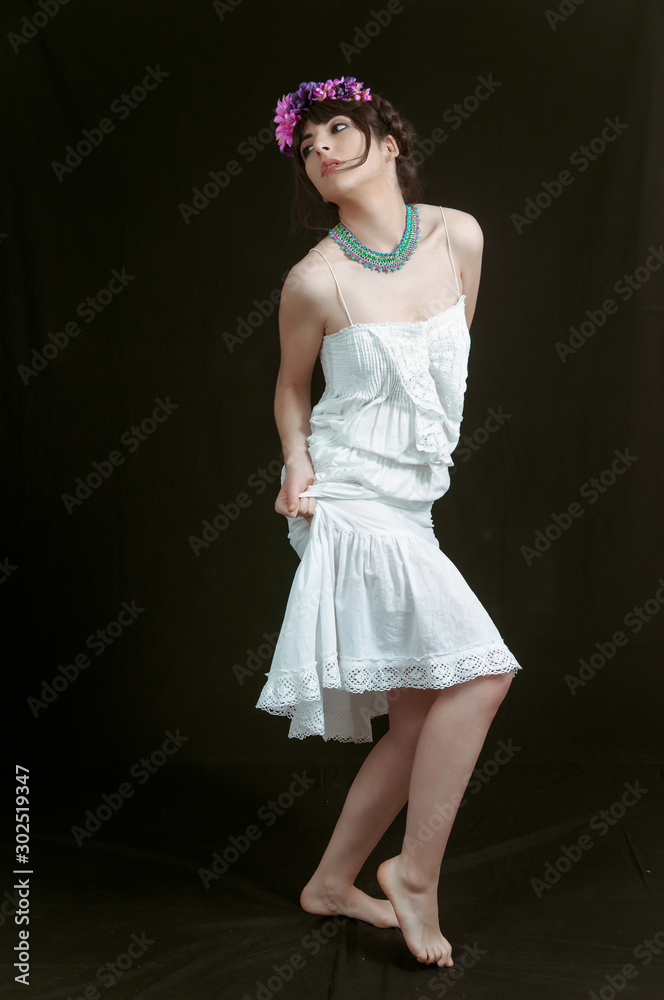 Young woman dancing with white dress and flowers in her hair. Black background.