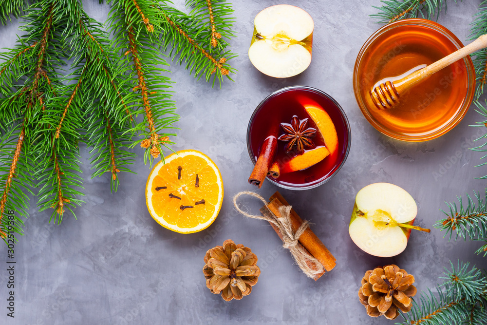 Mulled wine with spices in glass. Red mulled wine with cinnamon, anise and honey. Hot mulled wine at a cement gray background with fir branches and pine cones Mulled wine with spices in glass. Red mulled wine with cinnamon, anise and honey. Hot mulled wine at a cement gray background with fir branches and pine cones