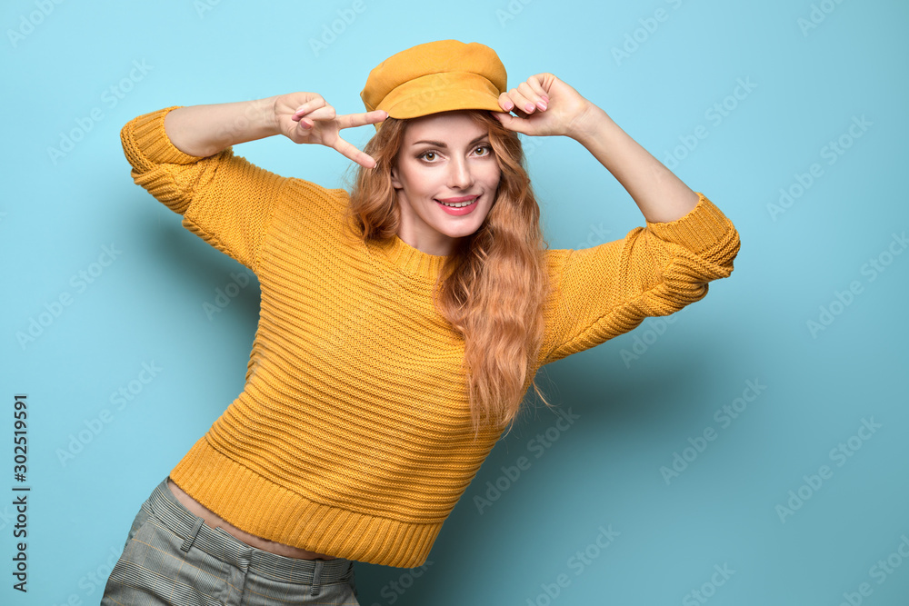 Easy-going Woman happy smiling in Stylish fashion yellow colored outfit. Beautiful young Girl in Trendy jumper, make up. Joyful lady shows peace sign in yellow cap, fashionable happiness concept Easy-going Woman happy smiling in Stylish fashion yellow colored outfit. Beautiful young Girl in Trendy jumper, make up. Joyful lady shows peace sign in yellow cap, fashionable happiness concept