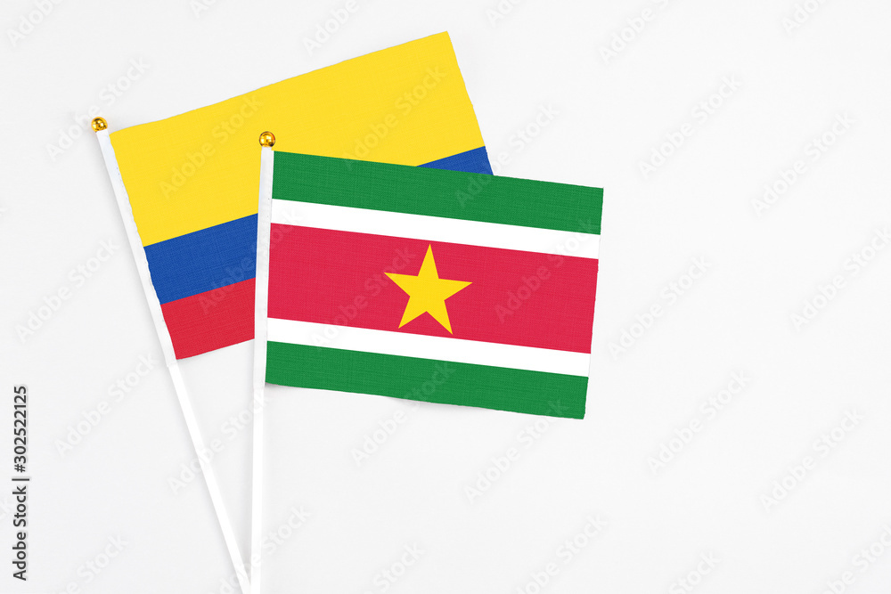Naklejka premium Suriname and Colombia stick flags on white background. High quality fabric, miniature national flag. Peaceful global concept.White floor for copy space.