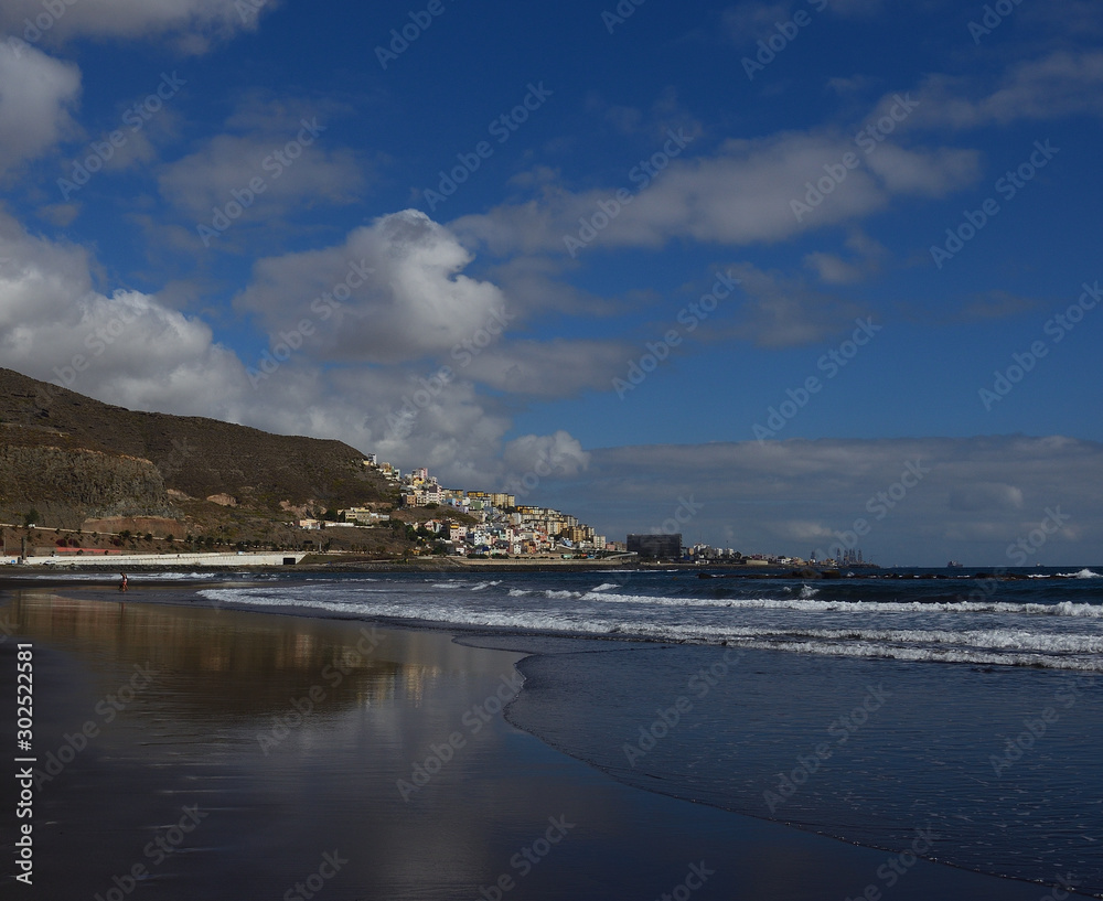 Sandy beach at low tide, city and blue sky with clouds, La Laja, coast of Las Palmas de Gran Canaria, Canary Islands