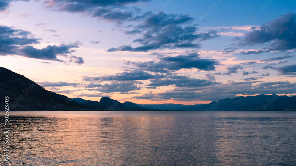 Beautiful sunset sky reflected in Okanagan Lake with view of distant mountains in summer